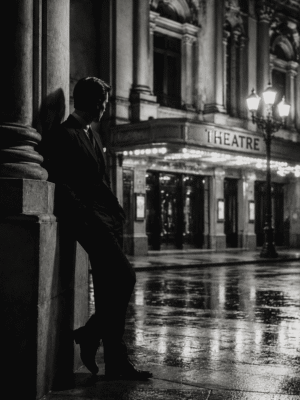 Midnight Theatre black and white film noir wall art print of a man in a suit leaning against a column outside a rain-lit theatre — digital download.