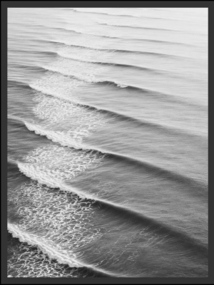 Main: Black and white aerial photograph of parallel ocean swells rolling toward shore, catching the light before dissolving into foam — fine art coastal wall art digital download. Short fallback: Black and white ocean swells wall art print.