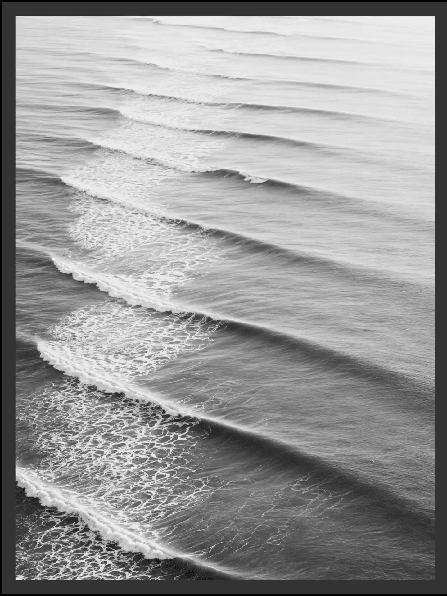 Main: Black and white aerial photograph of parallel ocean swells rolling toward shore, catching the light before dissolving into foam — fine art coastal wall art digital download. Short fallback: Black and white ocean swells wall art print.